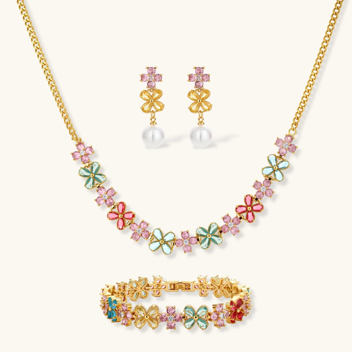 Gold-plated flower necklace, bracelet and drop earrings with multicolor zirconia petals and white round beads on a cream background.
