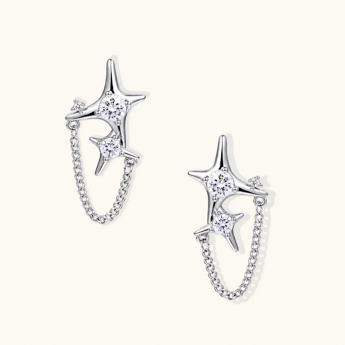 Silver star studs with crescent moon cutouts and zirconia stones connected by delicate chains on white background